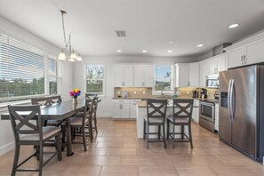 A modern kitchen with white cabinets, a stainless steel refrigerator, and a dining area with dark chairs and a light-colored table. - Walk to Lido Beach | Lower Game Room w/ Ping-Pong! (Sarasota)