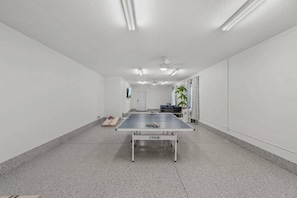 Ein Tischtennis-Tisch in einem Raum mit weißen Wänden, einem Deckenventilator und einer Tür im Hintergrund.