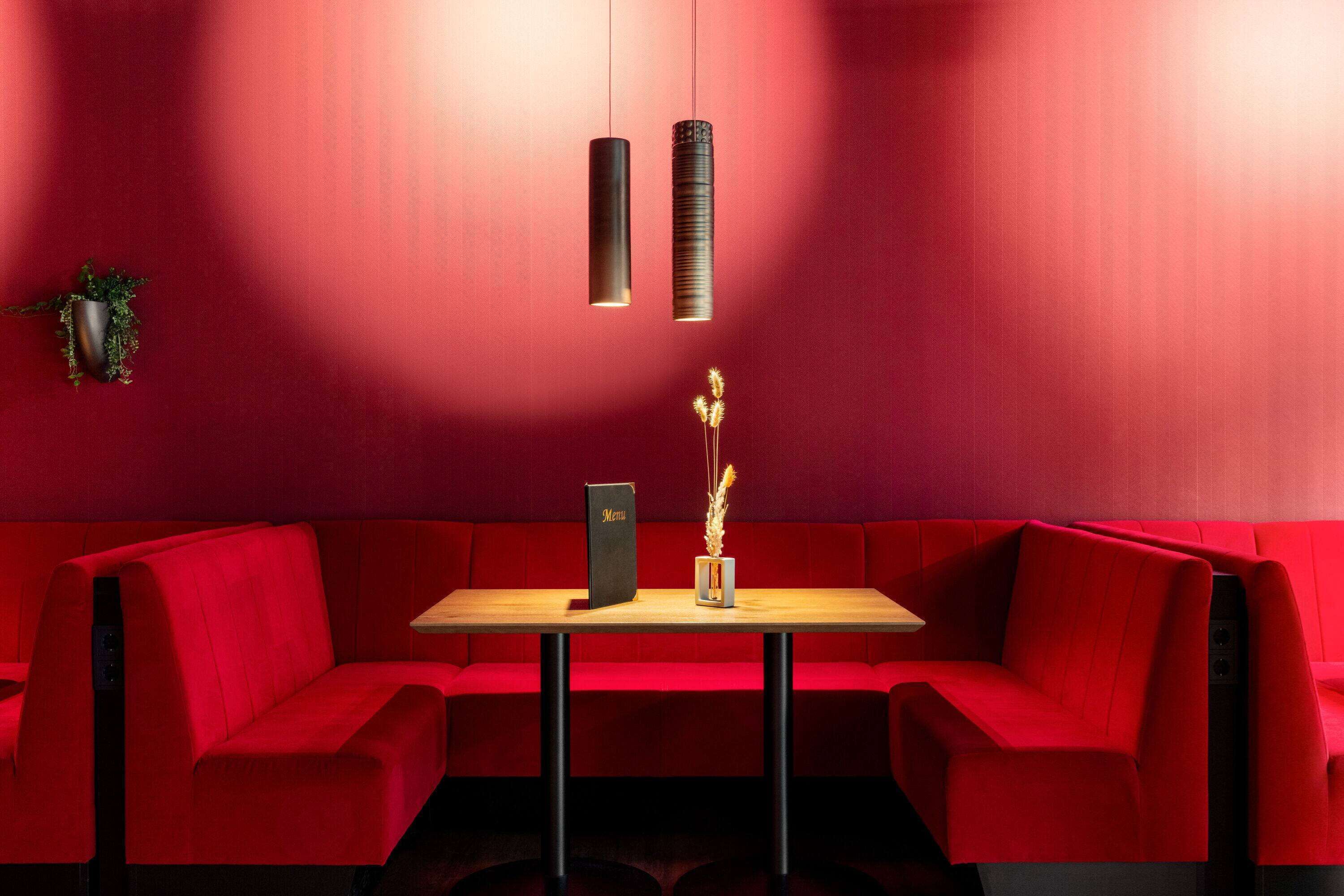 A red-themed restaurant with a wooden table and a menu stand, featuring a vase with dried plants.