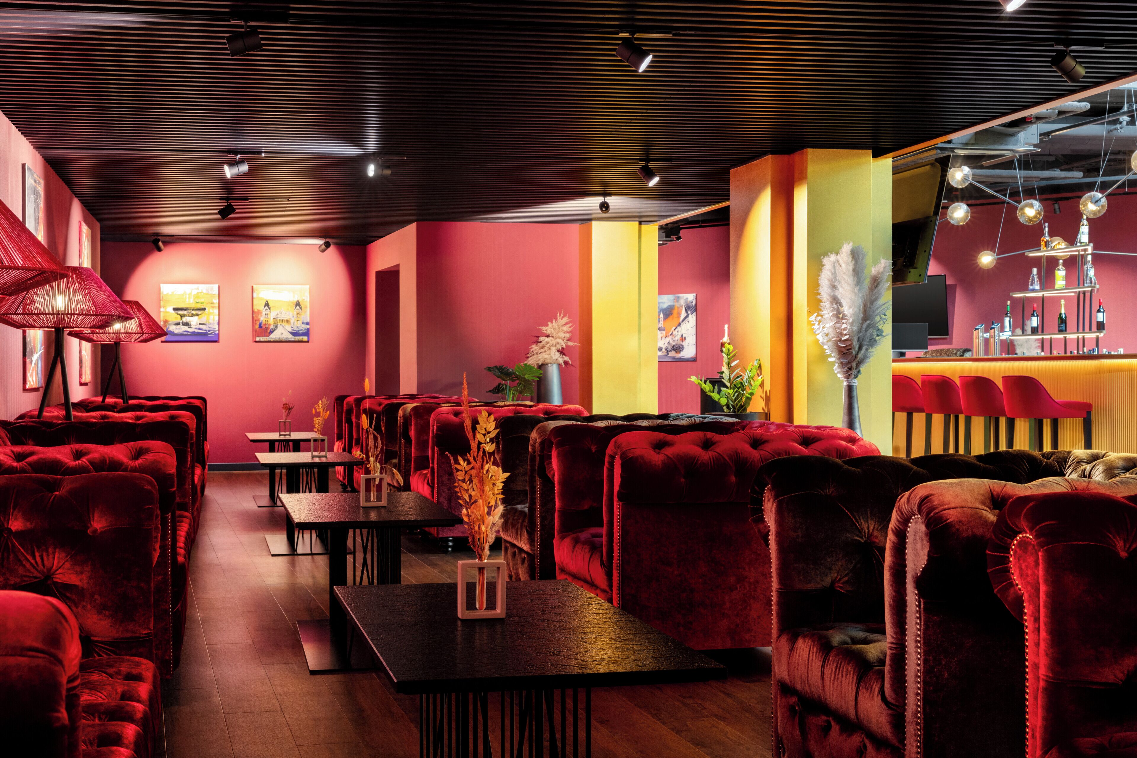 Un restaurante con asientos tapizados en rojo, mesas de madera y una zona de bar con un elemento decorativo de iluminación.