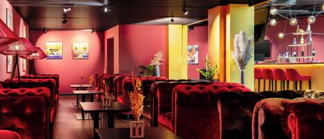 Un restaurante con asientos tapizados en rojo, mesas de madera y una zona de bar con un elemento decorativo de iluminación.
