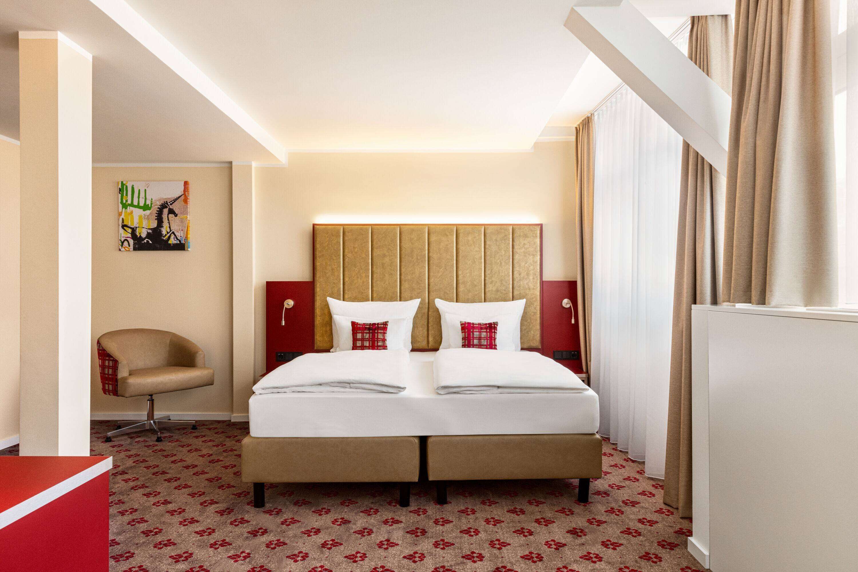 Habitación de hotel con cama doble, un sillón rojo, un cuadro en la pared y una alfombra roja.