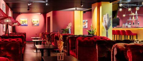A restaurant with red upholstered chairs, wooden tables, and a bar area with a modern light fixture.
