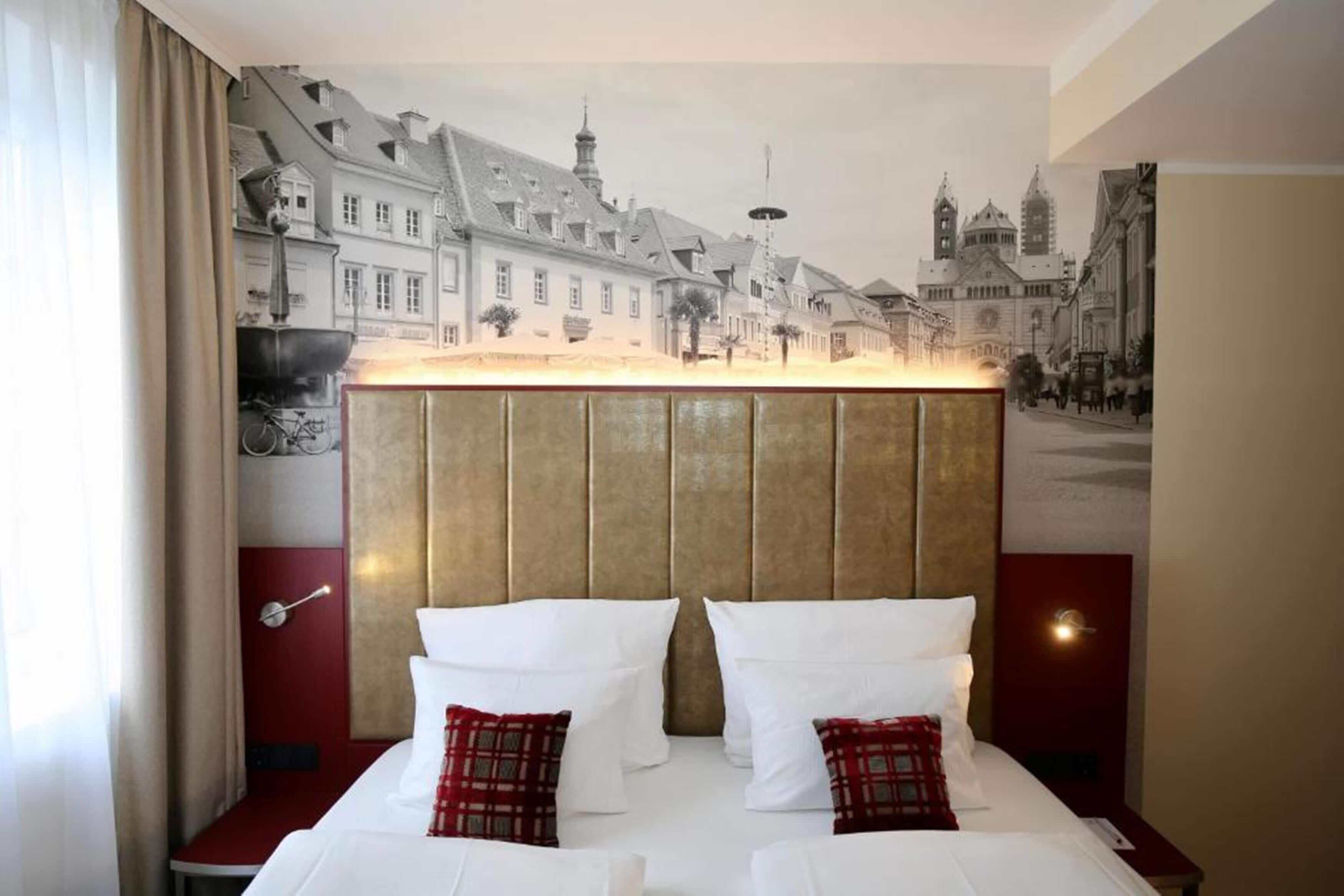 A hotel room with a large bed, a headboard with a cityscape mural, and a red accent wall.