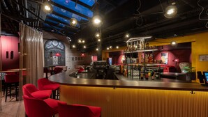 A bar area with a curved counter, red chairs, and a digital screen displaying multiple camera feeds. - Hotel Postgalerie Speyer (Speyer)