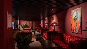 A red-themed lounge area with plush red sofas, a coffee table, and a large abstract painting on the wall. - Hotel Postgalerie Speyer (Speyer)