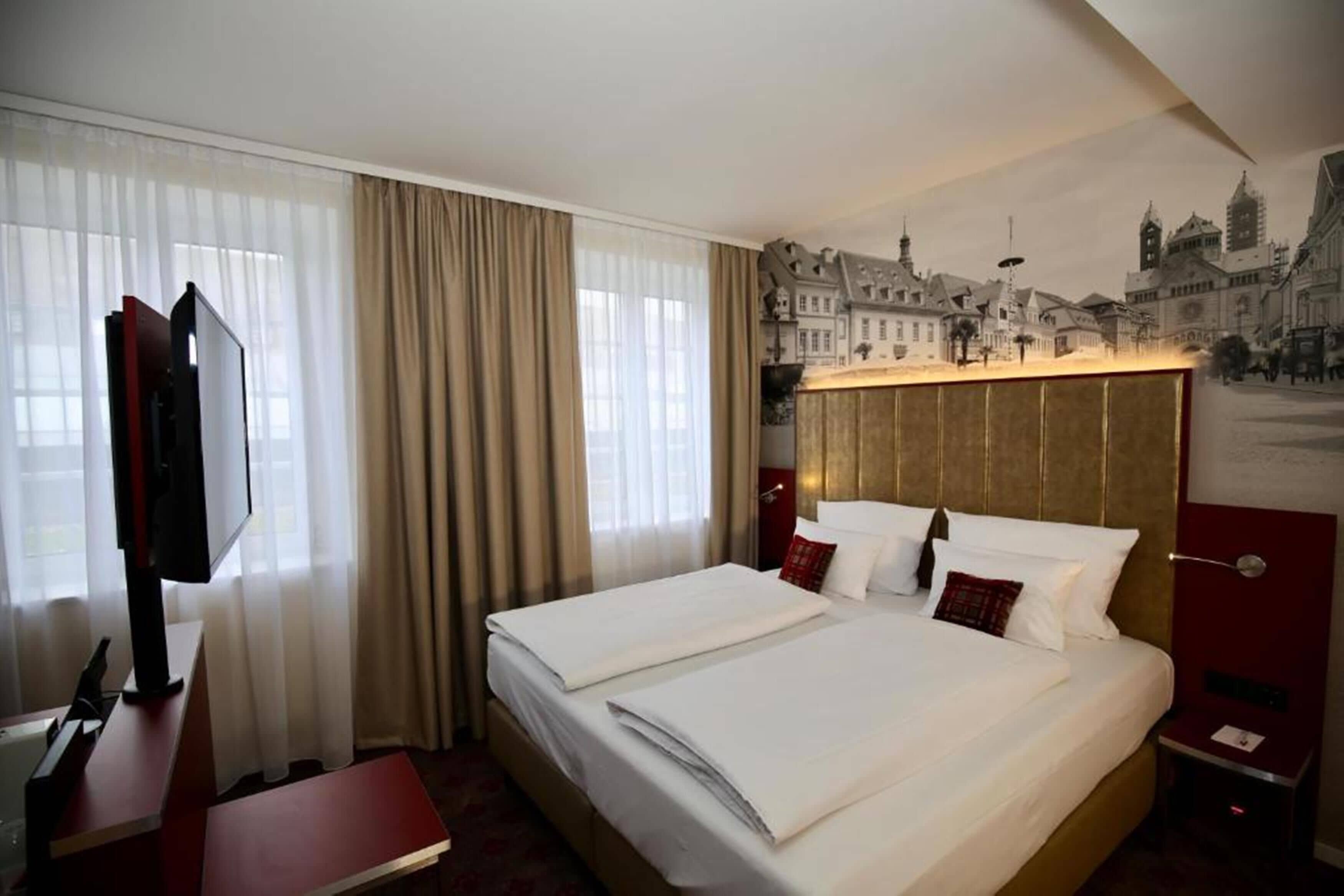 A hotel room with a large bed, a flat-screen TV, and a cityscape mural on the wall.