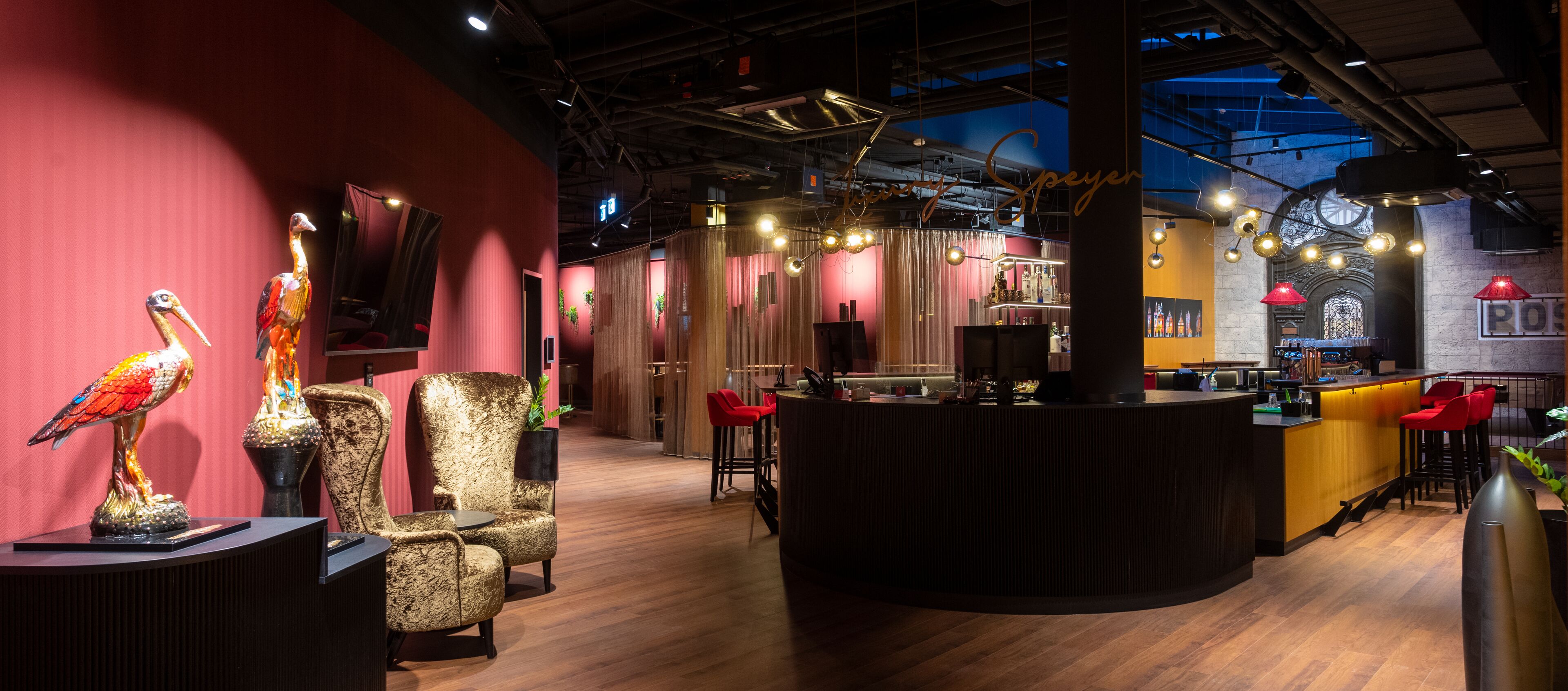 A modern bar area with a curved counter, red chairs, and decorative bird sculptures.