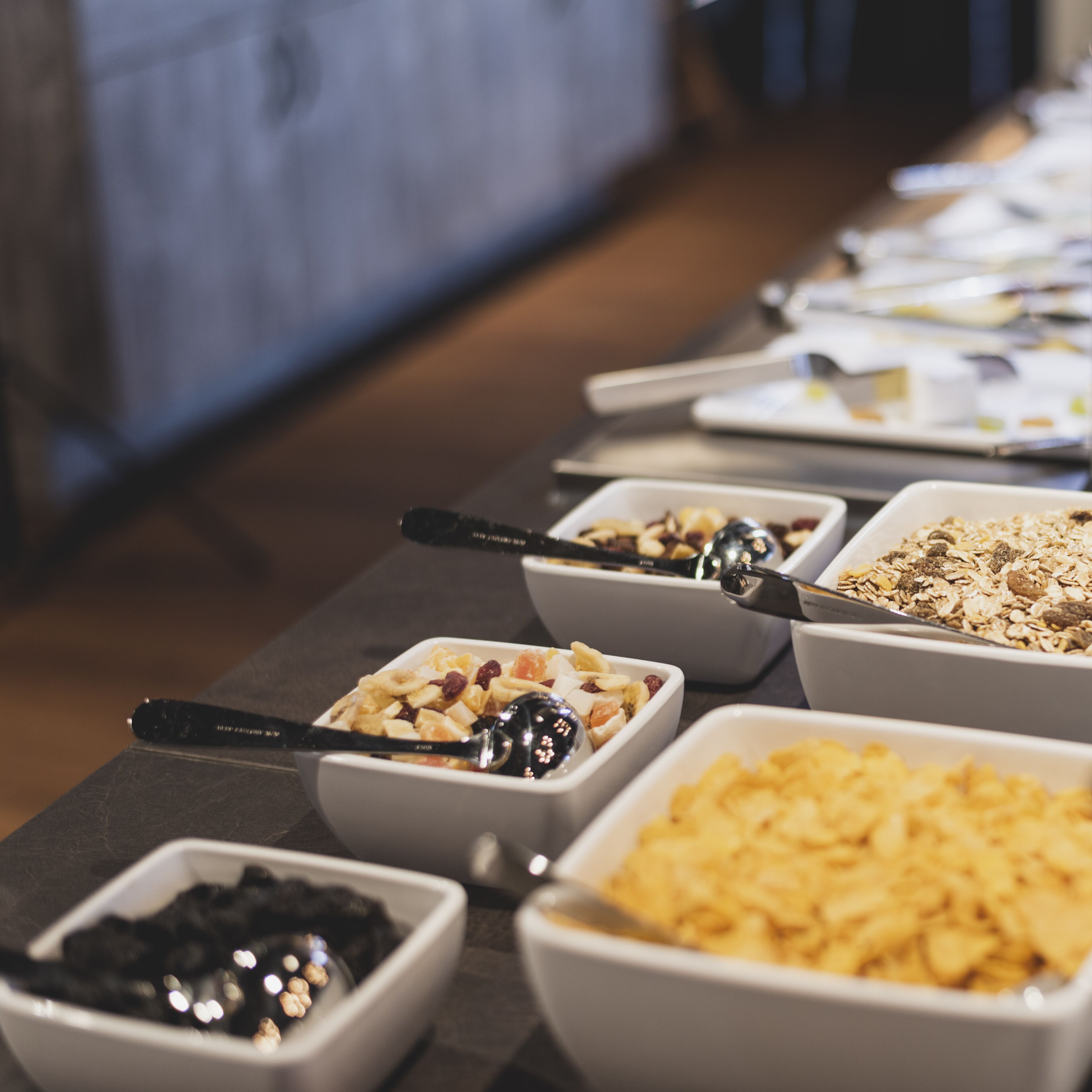 A buffet table with various food items in bowls, including fruits, nuts, and cereal.