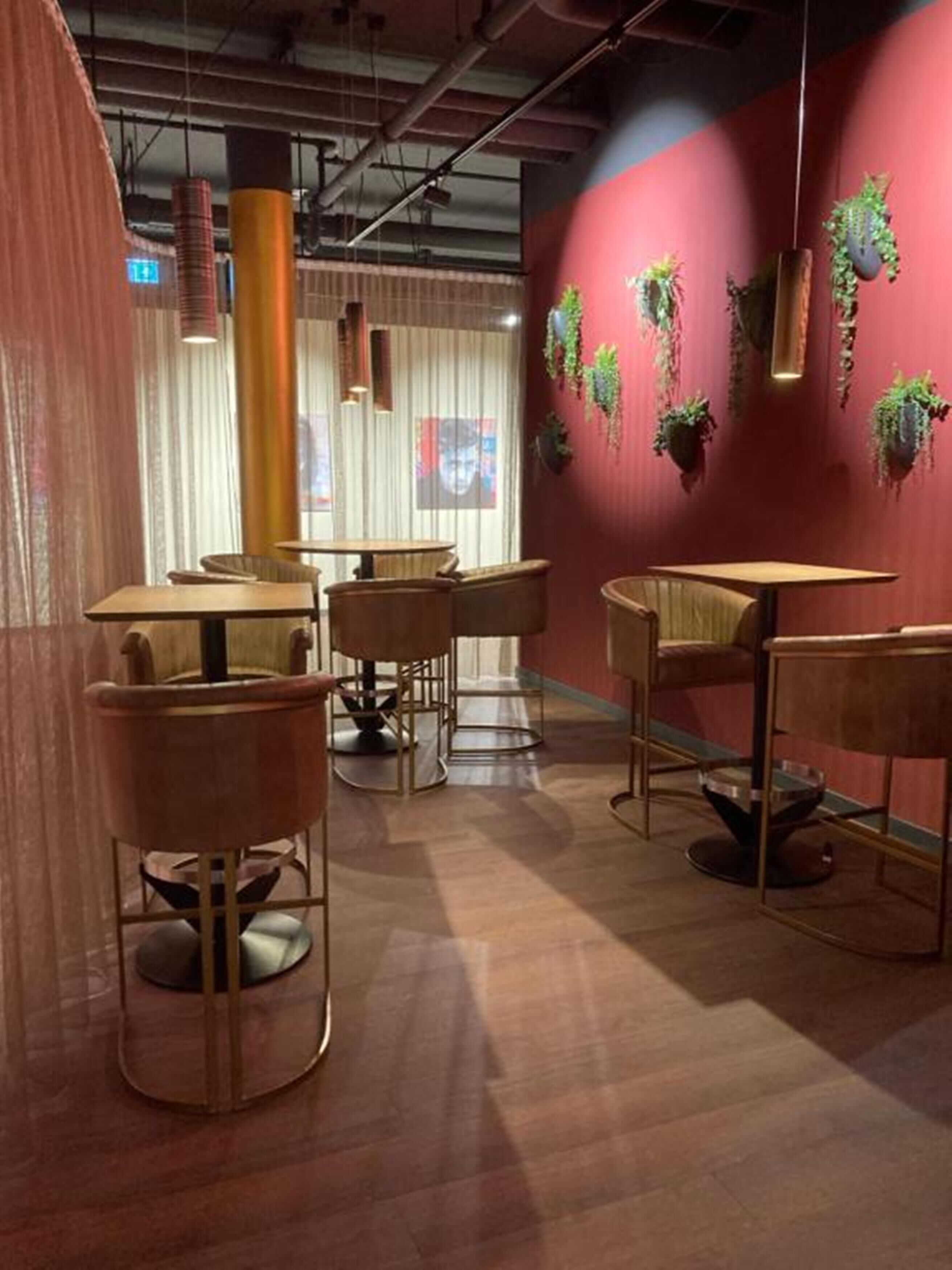 Un interior moderno con mesas y sillas redondas, una pared de acento roja y plantas colgantes.