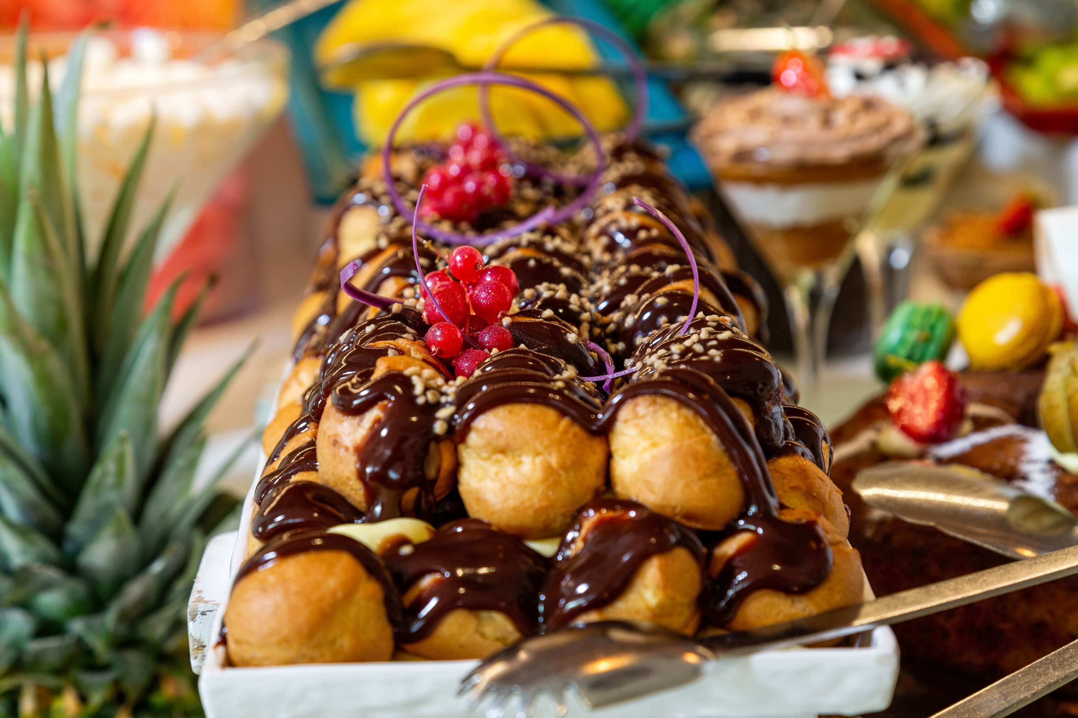 A dessert tray with chocolate-dipped profiteroles, garnished with red berries and nuts.