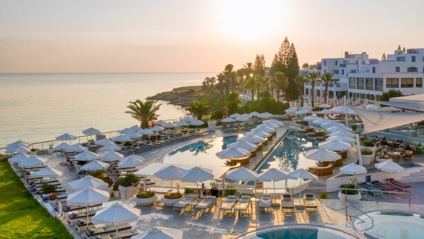 A resort with a pool area, sun loungers, umbrellas, and a view of the sea. - King Jason Protaras - Designed for Adults By Louis Hotels (Paralimni)
