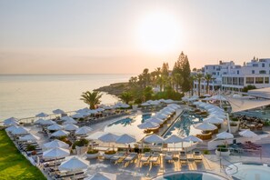 A resort with a pool area, sun loungers, umbrellas, and a view of the sea. - King Jason Protaras - Designed for Adults By Louis Hotels (Paralimni)