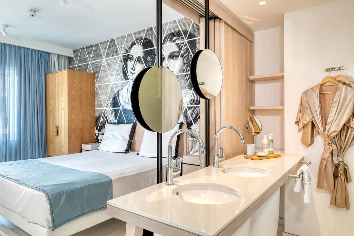 A modern hotel room with a large bed, a double sink, and a mirror.