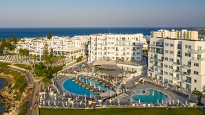 A resort with multiple white buildings, a large central pool, and a view of the sea. - King Jason Protaras - Designed for Adults By Louis Hotels (Paralimni)