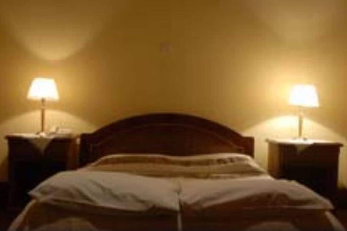 Habitació d'hotel amb un llit, dues làmpades de nit i un panell de capçal de fusta.