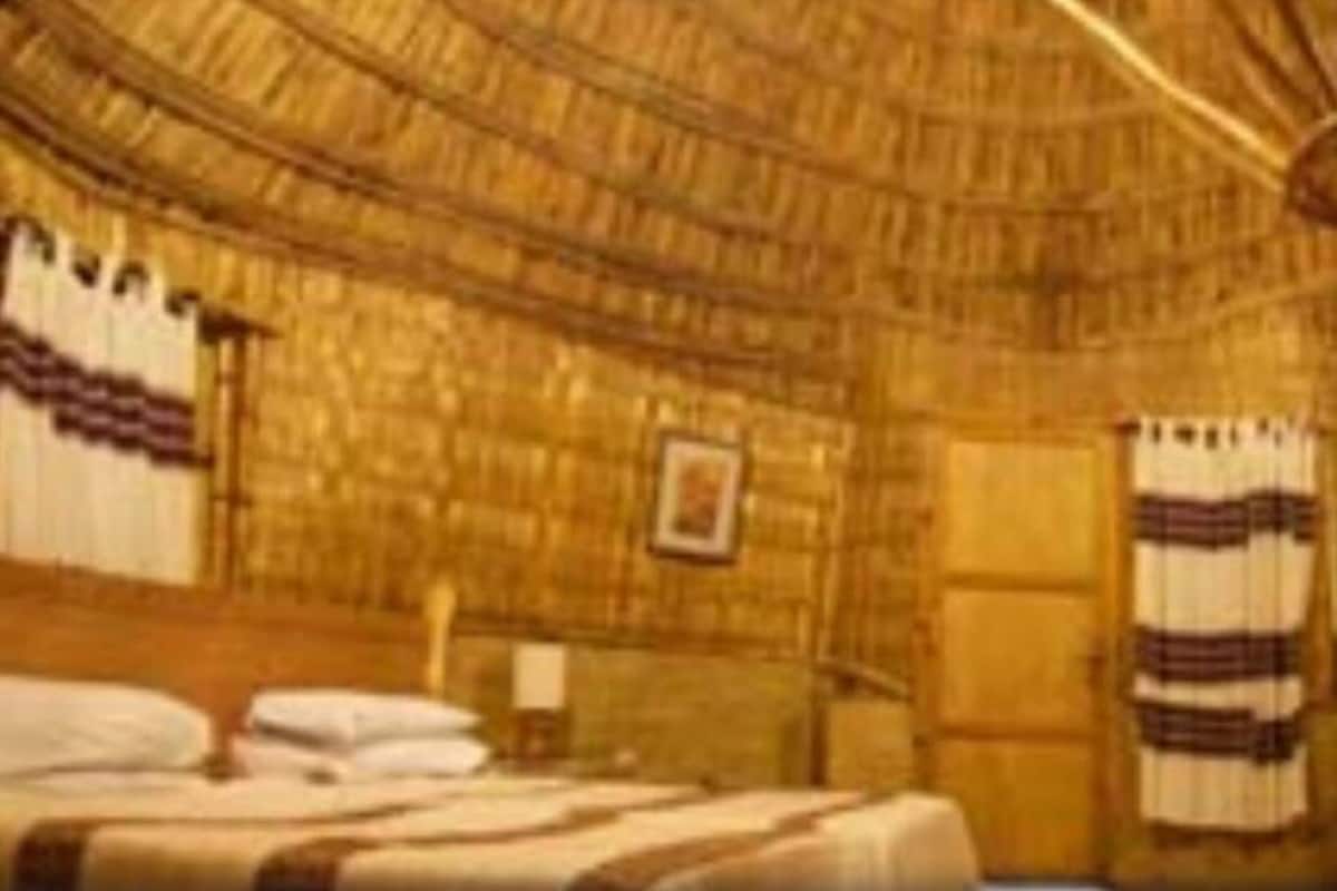 Una habitació amb un teulat de palla, un llit amb col·cha ratllada i un quadre al mur.
