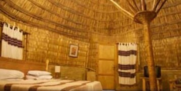 Una habitación con techo de paja, una cama con colcha a rayas y un cuadro en la pared.