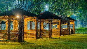 Una serie de estructuras de madera con lados abiertos, posiblemente un pabellón o mirador, ubicadas en un área con césped y árboles al fondo.