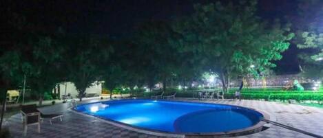 Una piscina con suelo a cuadros, rodeada de árboles y una zona bien iluminada.