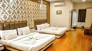 Habitación de hotel con dos camas, piso de madera, papel tapiz estampado, unidad de aire acondicionado y un pequeño cuadro en la pared.