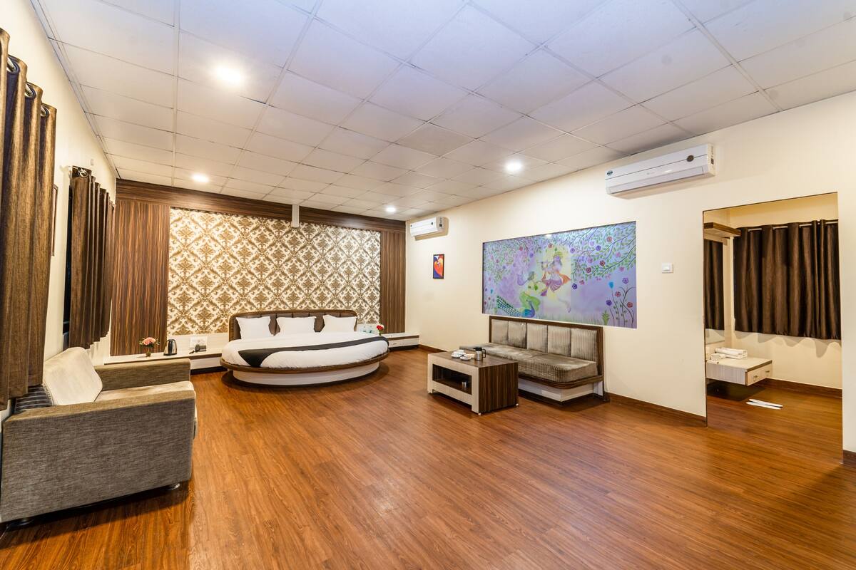 A modern hotel room with a circular bed, a sofa, a small coffee table, and a large abstract painting on the wall.