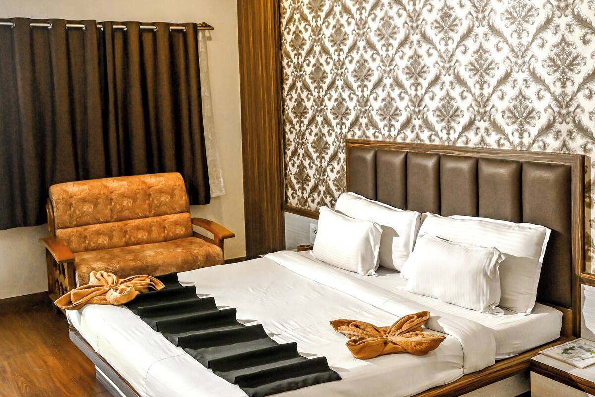 A hotel room with a large bed, a wooden headboard, a brown armchair, and a patterned wallpaper.