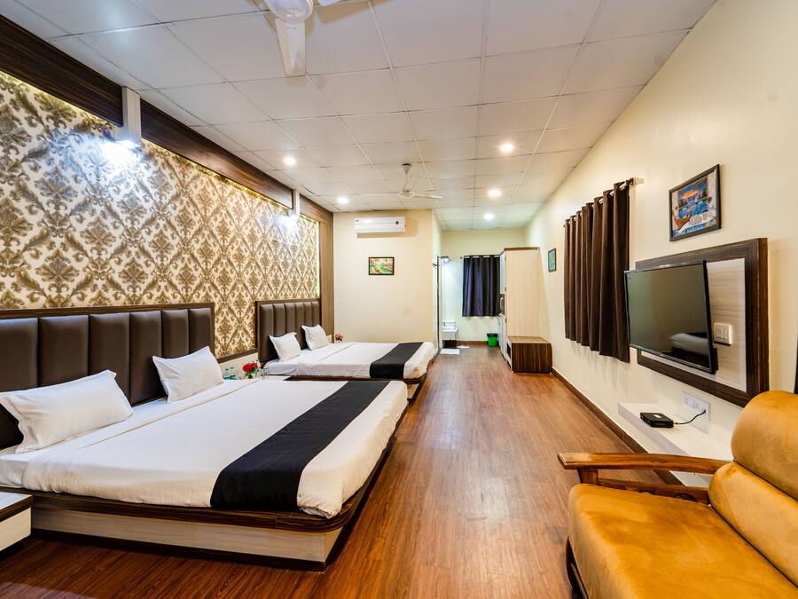 A hotel room with two beds, a TV, a sofa, and a wooden floor.