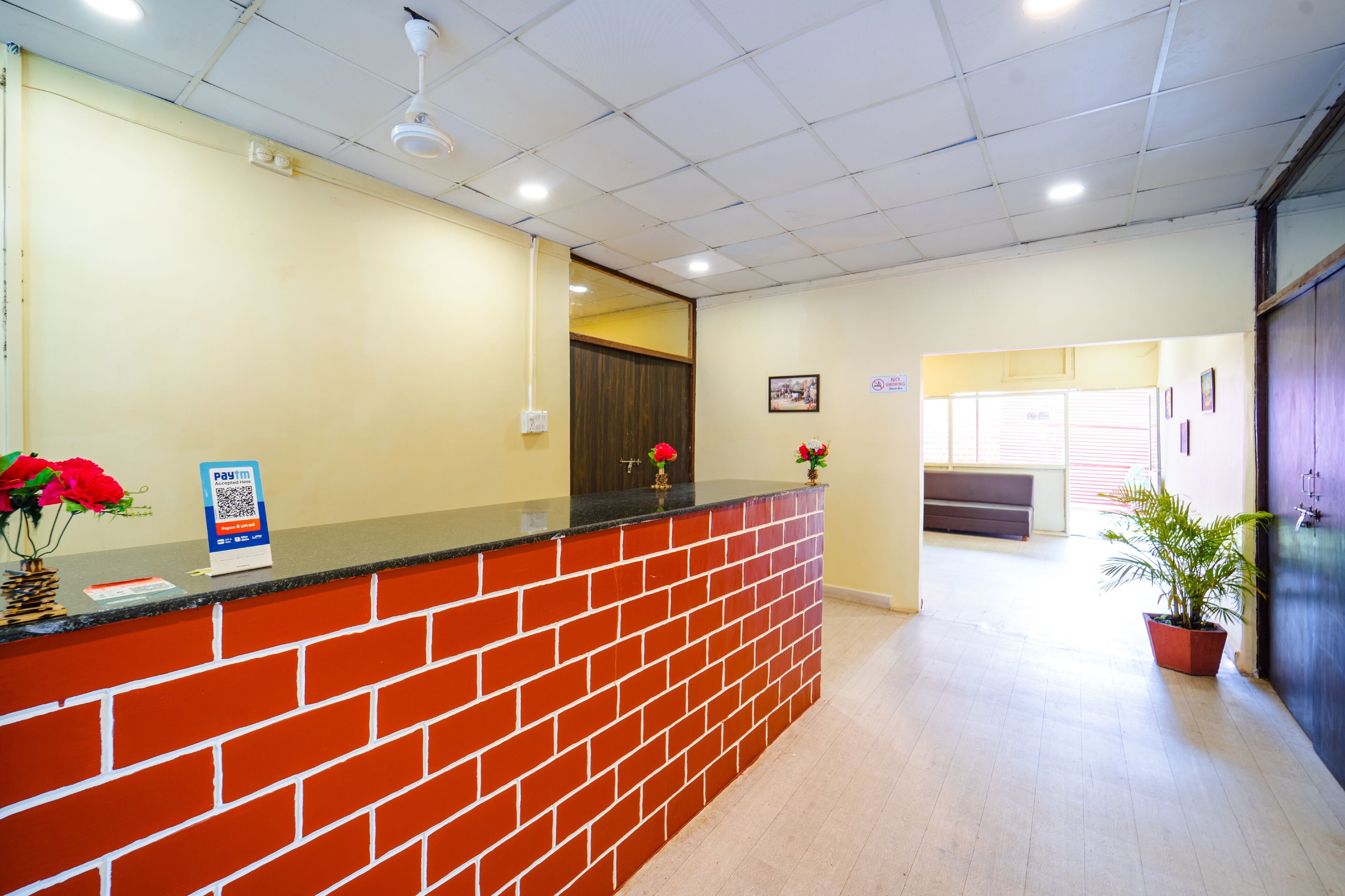 Zona de recepción con mostrador de ladrillo, estación de pago con código QR y planta en maceta.
