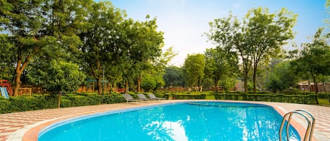 Una piscina con borde de baldosas, rodeada de árboles y un cielo despejado.
