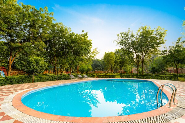 Una piscina con borde de baldosas, rodeada de árboles y un cielo despejado.