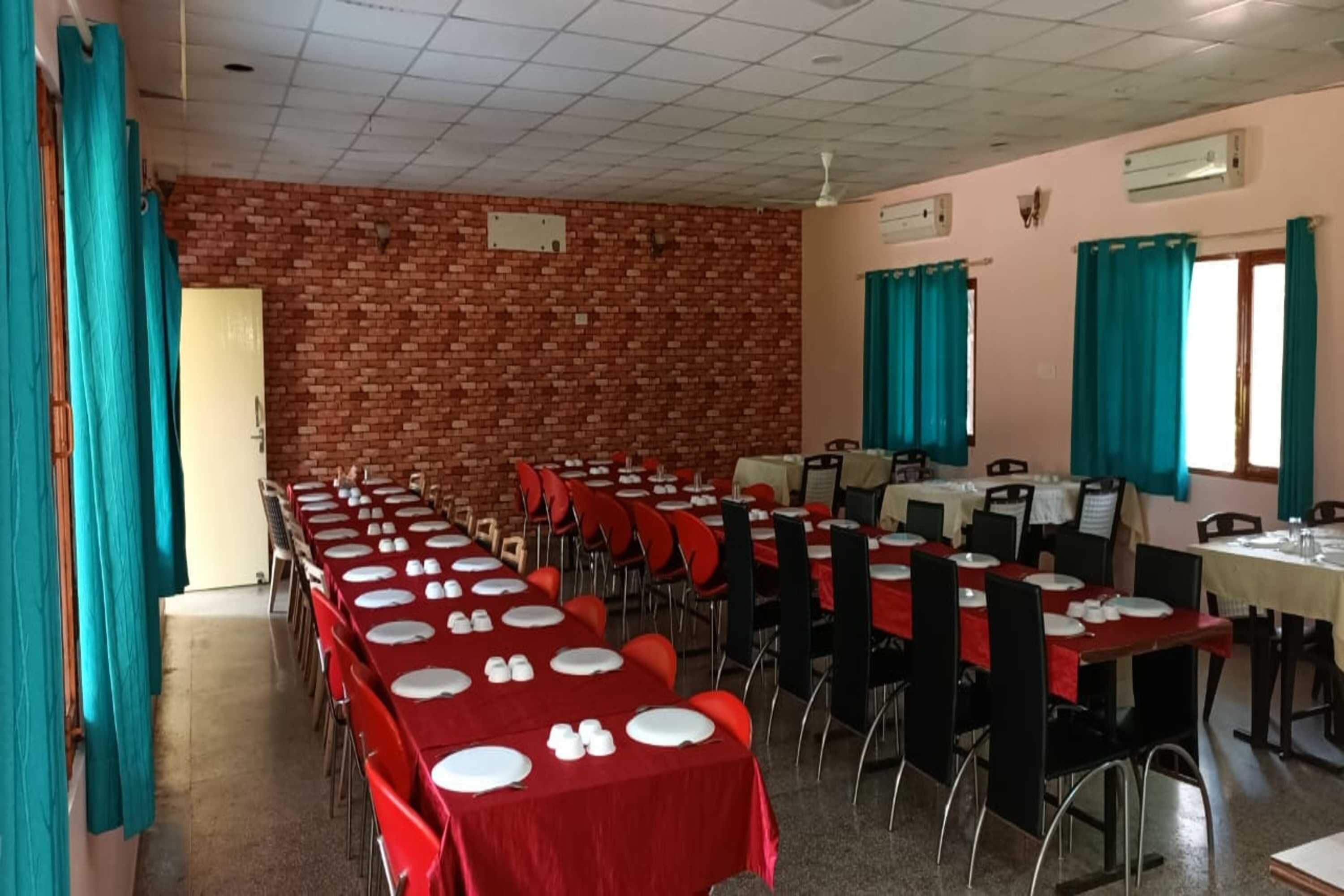 A dining hall with brick walls, multiple tables with red tablecloths, and teal curtains.