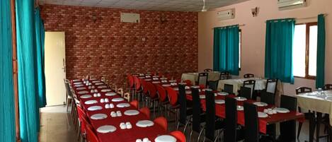 A dining hall with brick walls, multiple tables with red tablecloths, and teal curtains.