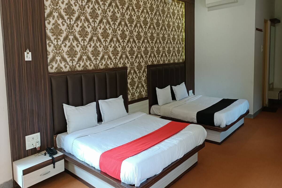A hotel room with two beds, a wooden headboard, a patterned wallpaper, and a red bed runner.
