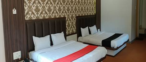 A hotel room with two beds, a wooden headboard, a patterned wallpaper, and a red bed runner.