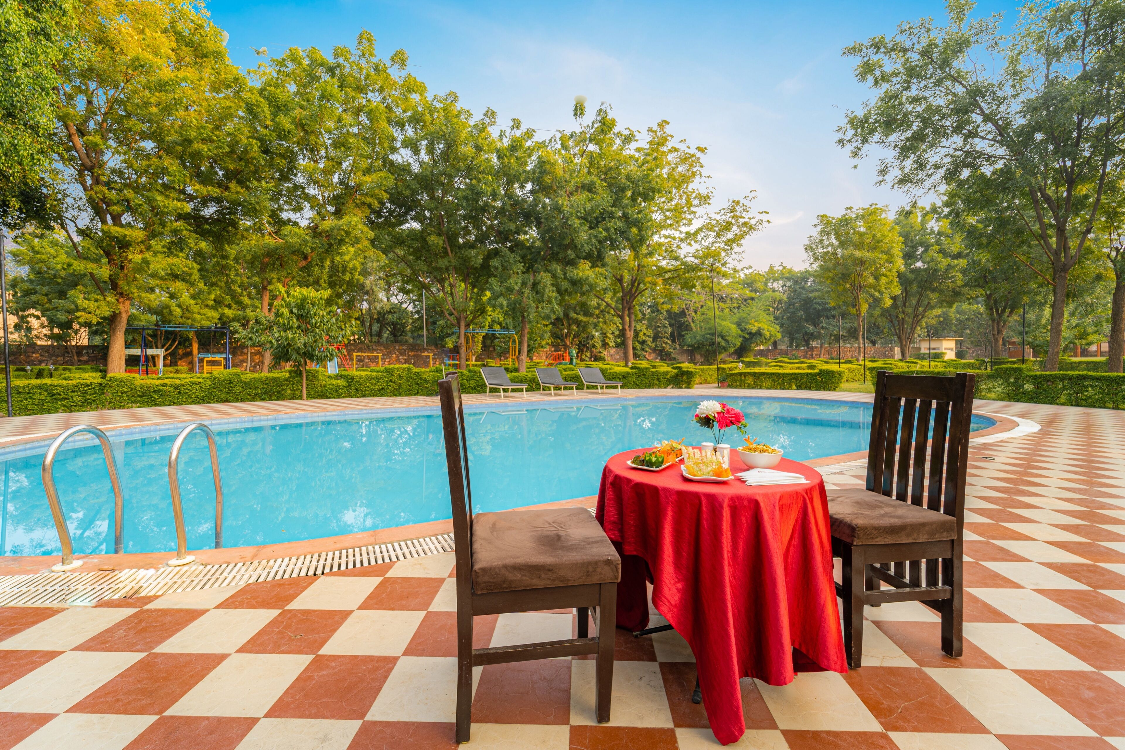 A poolside area with a checkered floor, a table with a red tablecloth, and two chairs.