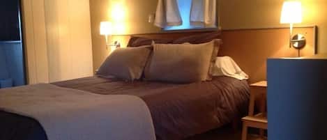 Ein ordentlich bezogenes Bett mit Kopfteil, zwei Nachttischlampen und einem Fenster mit Vorhängen.