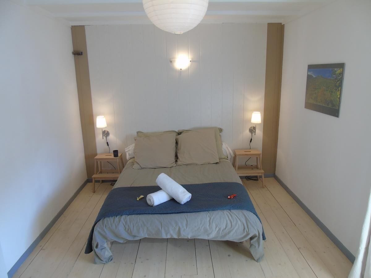 A bedroom with a bed, two bedside lamps, a wall-mounted light, and a painting.