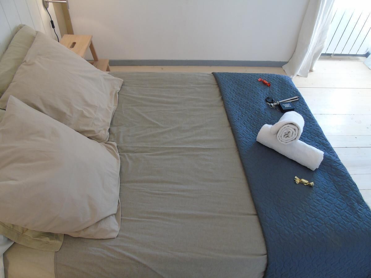 Una cama con colchón gris, almohadas color beige y una manta azul.