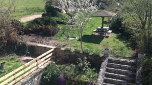 Un jardín con muro de piedra, banco de madera y un pabellón.