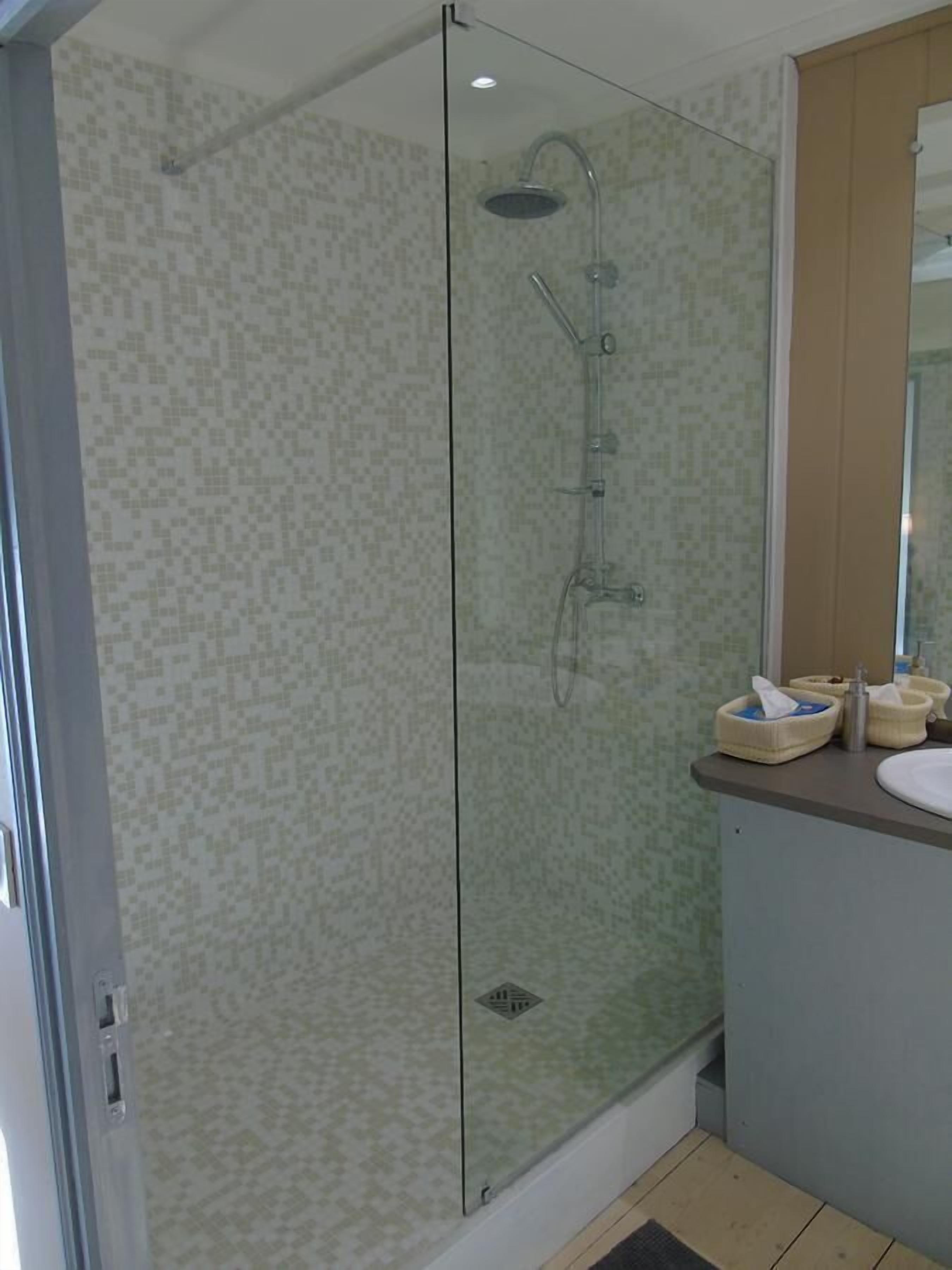 A glass-enclosed shower with a handheld showerhead and a wall-mounted faucet.