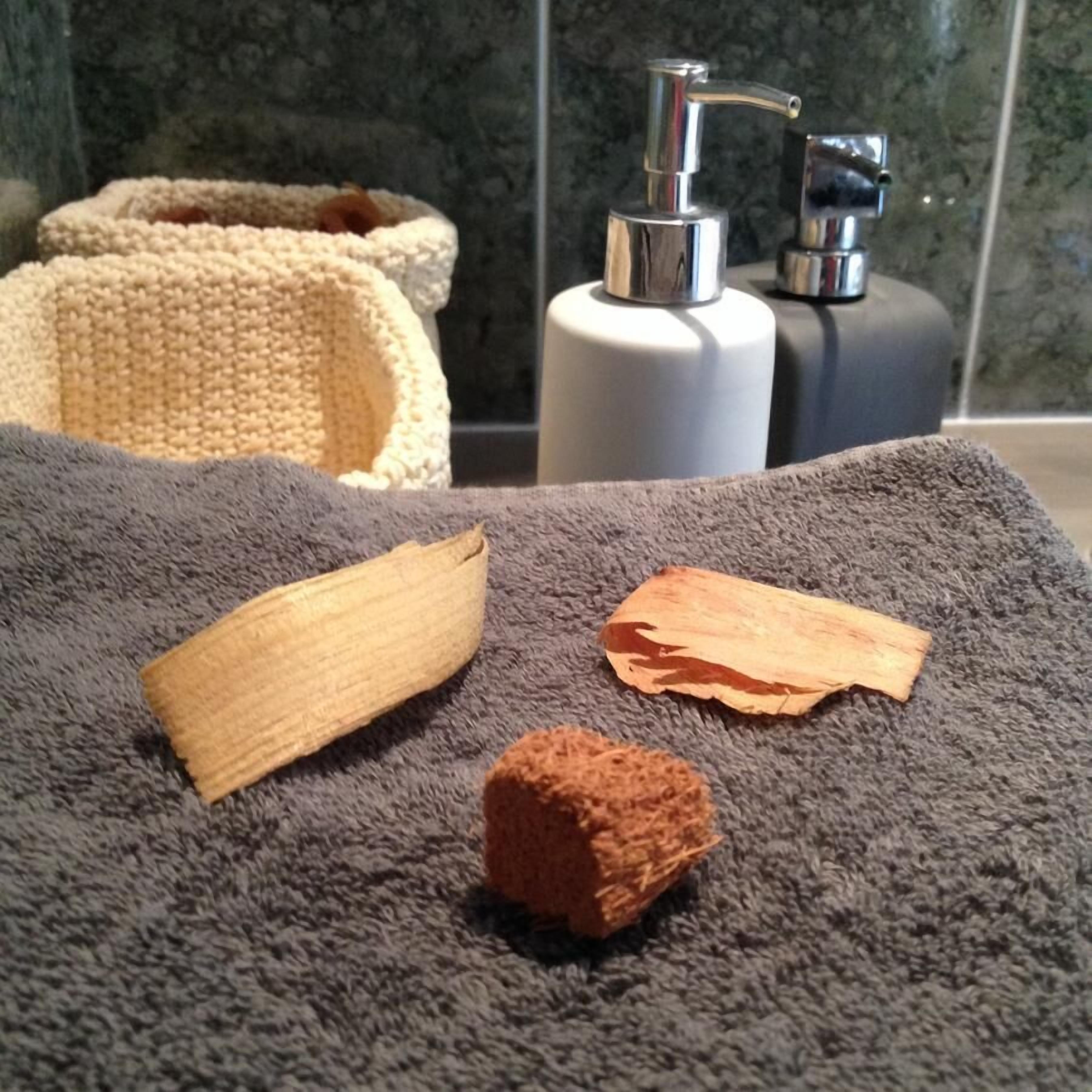 Une salle de bain avec une serviette grise, un objet en bois et une éponge marron posés dessus.