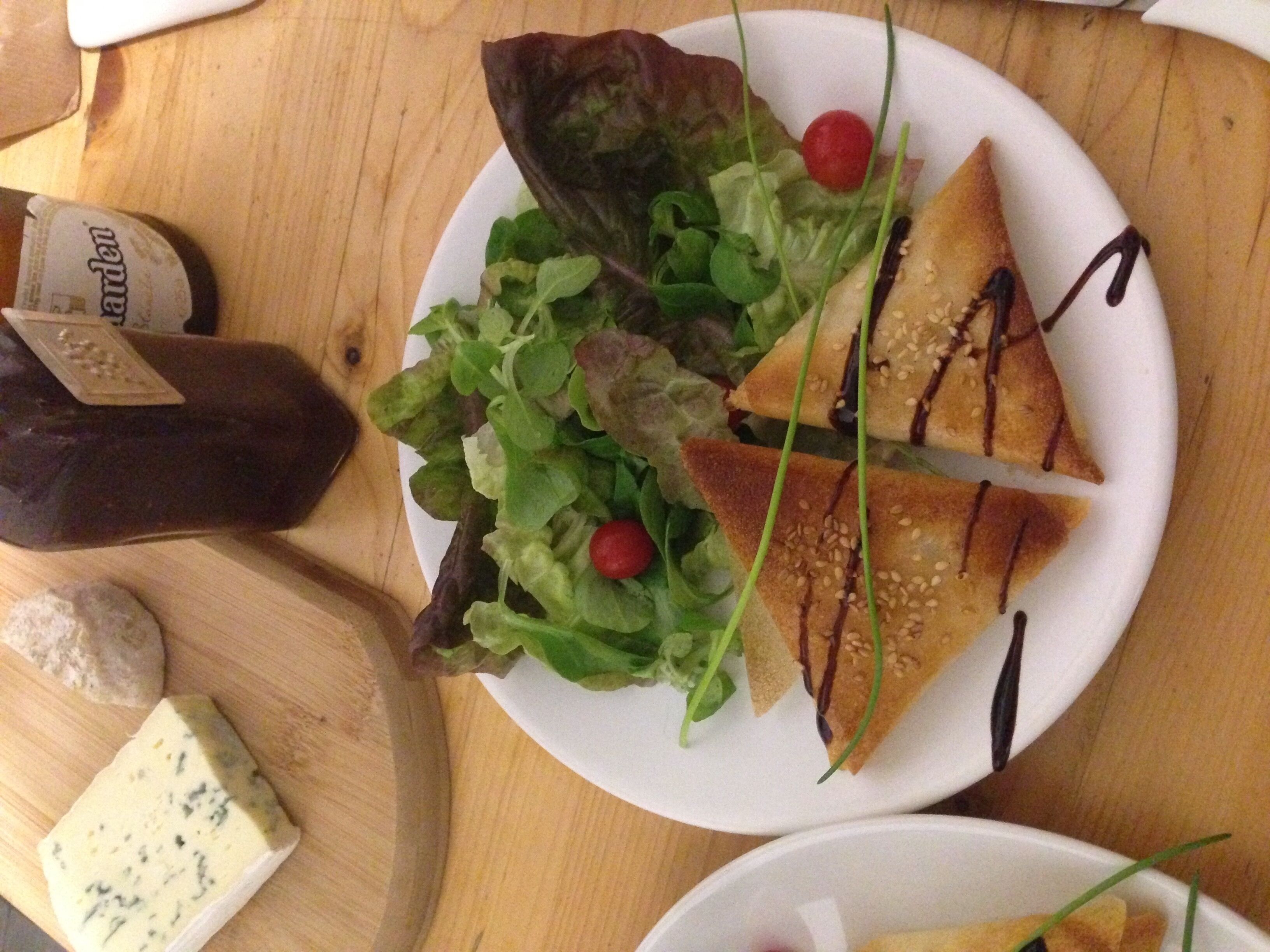 Une assiette avec une salade, un morceau de fromage et une bouteille de vinaigrette.