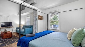 Une chambre à coucher avec un lit, une télévision, un canapé et une fenêtre avec des stores.