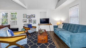 Un salon avec un canapé bleu, deux fauteuils, une table basse et un téléviseur posé sur un meuble.