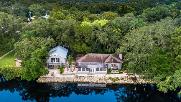 Une vue aérienne d’une maison entourée d’une forêt dense et bordée d’un plan d’eau.