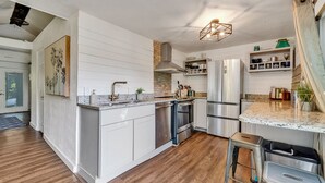 Une cuisine moderne avec des meubles blancs, un plan de travail en granit, des appareils électroménagers en acier inoxydable et un plancher en bois.
