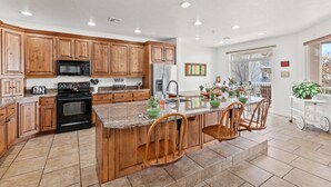 Une cuisine spacieuse avec des meubles en bois, un îlot central doté de chaises, un four à micro-ondes et un réfrigérateur.