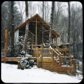 Een houten chalet met een veranda en trap, omringd door met sneeuw bedekte bomen.