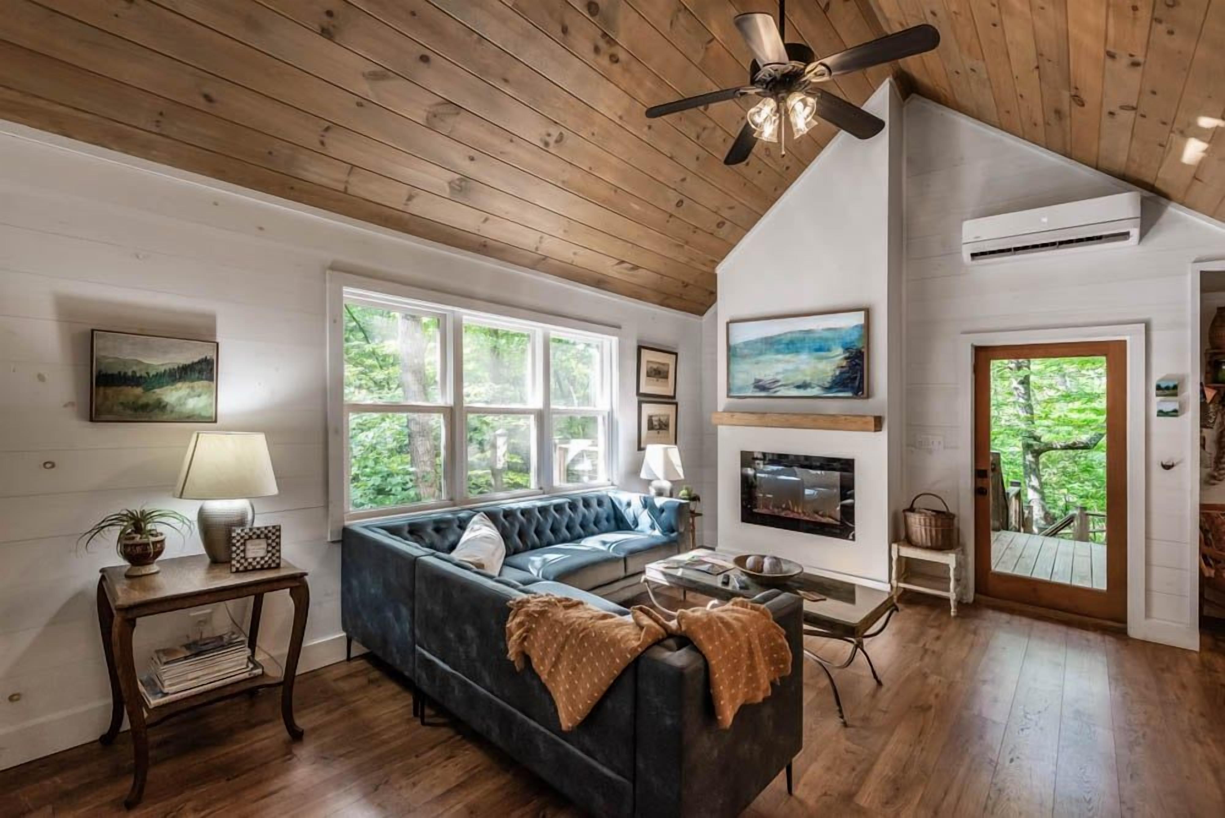 A cozy living room with a dark blue sofa, wooden flooring, a ceiling fan, and a fireplace.